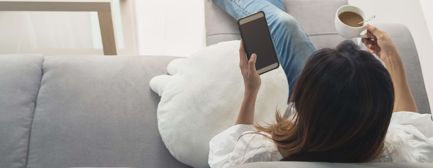 a person siting on a couch holding a phone and a coffee